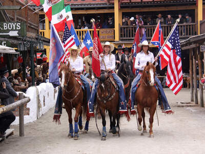 Eine Gruppe von Menschen reitet auf Pferden durch die Straßen von Pullman City Western town im Bayerischen Wald.