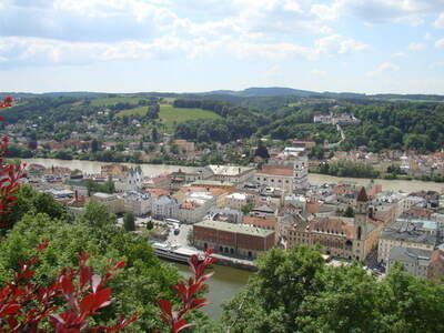 Luftaufnahme von Schärding mit Fluss Inn, historischen Gebäuden und umliegenden Hügeln.